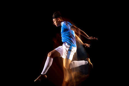 Young sportsman, soccer football player training isolated over black background in mixed light....