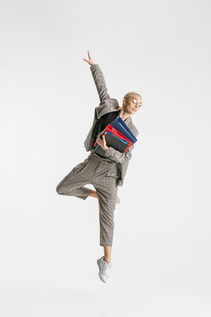 Full-length portrait of female employee in classical suit with folder jumping like ballerina...
