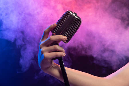 Close-up image of stage microphone in female hands isolated over gradient blue purple background in...