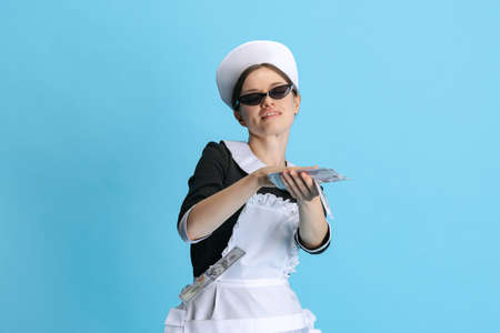 Bossy young woman in chambermaid uniform and stylish sunglasses isolated over blue backgroundの写真素材