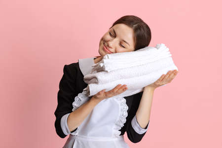 Portrait of young Caucasian chambermaid with clean towels isolated over pink backgroundの写真素材