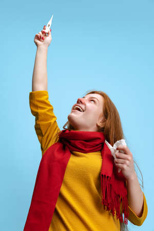 Portrait of young excited girl recovering from a cold, measuring temperature isolated over blue background.の写真素材