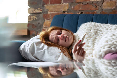 Cropped portrait of young girl feeling sick, having cold, flu lying on sofa and measuring...
