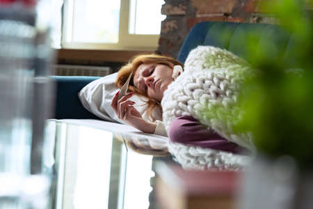 Cropped portrait of young girl lying on sofa, measuring temperature. Feeling sick.の写真素材