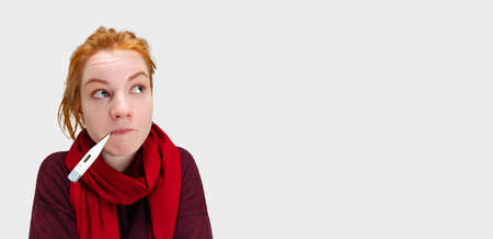 Cropped portrait of young Caucasian girl feeling sick and measuring temperature with electronic thermometer isolated over white backgroundの写真素材