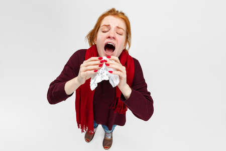 Portrait of young girl having a cold and flu, sneezing into napkin isolated over white background. Seasonal illness, allergyの写真素材
