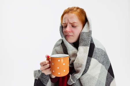 Cropped portrait of young girl wearing big warm scarf, feeling sick and drinking tea isolated over white background. Seasonal illnessの写真素材