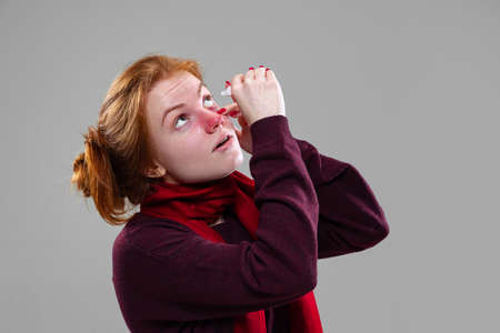 Cropped portrait of young girl dripping the eye drops isolated over gray background. Seasonal allergyの写真素材
