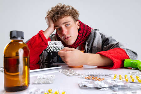 Portrait of ill boy, suffering from cold and flu surrounded by pills isolated over gray background. Self-isolationの写真素材