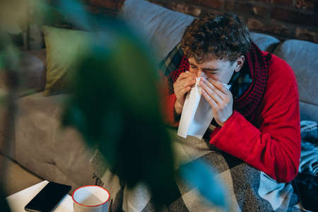 Cropped portrait of young sick boy having hold and flu, allergy. Sneezing, running noseの写真素材