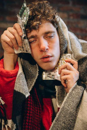 Cropped portrait of young tired sick boy holding pills. Cold and flu, allergy. Medical treatment