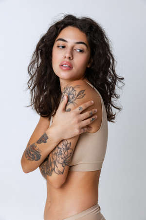 Cropped portrait of tender, beautiful young woman in beige inner wear isolated over gray backgroundの写真素材