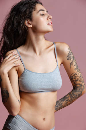 Cropped portrait of beautiful young woman in gray inner wear posing isolated over pink background. Natural beauty, body positivityの写真素材