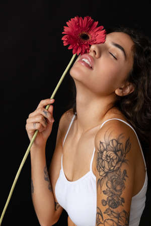 Cropped close-up portrait of beautiful tender woman with red gerberas posing isolated over dark backgroundの写真素材