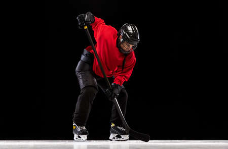 Full-length portrait of professional female hockey player training, dribbling puck isolated over black background.の写真素材