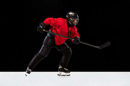 Full-length side view portrait of woman, professional hockey player in motion, training isolated over black background. High sticking gameの写真素材