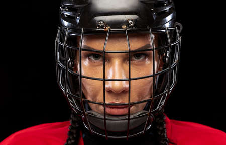 Close-up portrait of professional female hockey player in special protective helmet isolated over black background. High motivationの写真素材