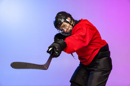 Cropped portrait of professional female hockey player training in special uniform with helmet isolated over gradient blue purple background.の写真素材