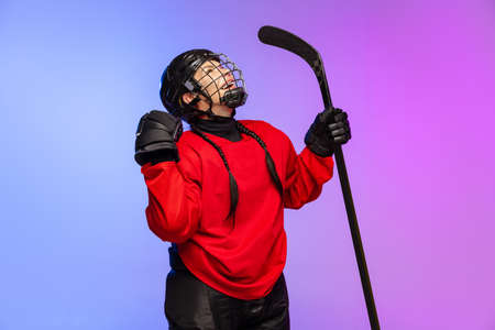 Portrait of professional female hockey player in special protective helmet isolated over gradient blue purple background. High motivationの写真素材