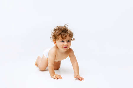 Portrait of little cute toddler boy, baby in diaper crawling isolated over white studio backgroundの写真素材