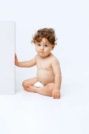 Portrait of little sweet toddler boy, baby in diaper calmly sitting isolated over white studio backgroundの写真素材