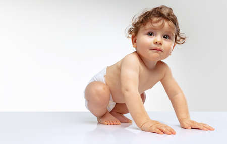 Portrait of toddler boy, baby in diaper calmly crawling isolated over white studio background....
