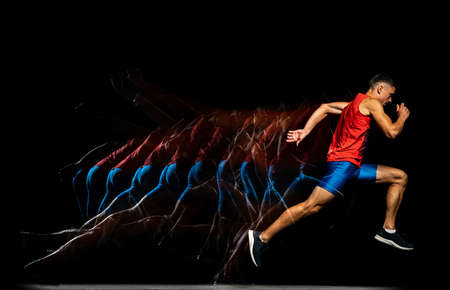Full-length portrait of young male athlete, professional runner in motion isolated over black...