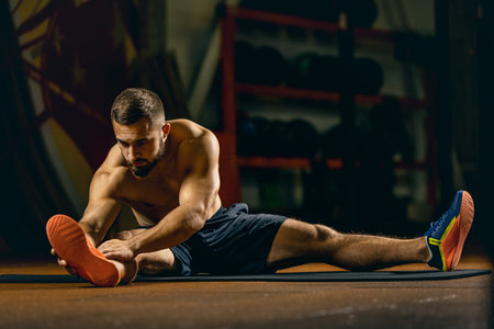 Full-length portrait of young sportive man doing stretching. Gym training