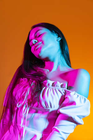 Beautiful portrait of atrractive young girl passionately dancing isolated over orange background in...