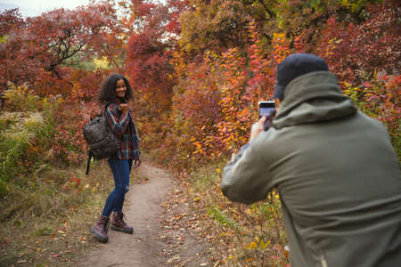 Cropped image of man doing photo of young beautiful girl isolated over colorful autumn landscape....