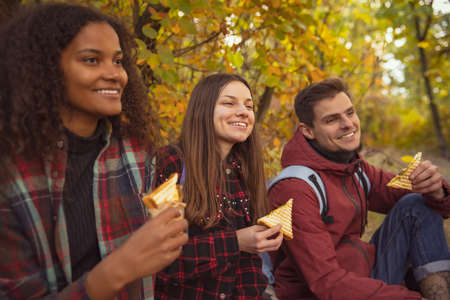 Cropped portrait of young people, friends having picnic, eating sandwiches in the autumn forest