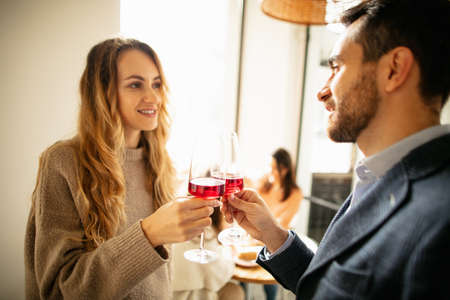 Cropped portrait of young beautiful couple having brunch at cafe, drinking red wineの写真素材