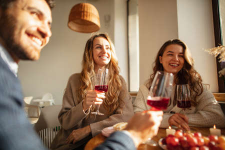Cropped portrait of joyful friends sitting at cafe, enjoying drinking wine. Sunny day meetingの写真素材