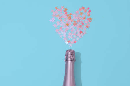 Champagne bottle with heart shape confetti design lying on blue paper background. Valentines Day celebration celebrationの写真素材
