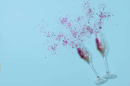 Two champagne flute with confetti inside lying on blue paper background. New Year celebration