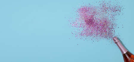 Champagne bottle with with confetti splashes lying on blue paper background. Valentines Day celebration celebrationの写真素材