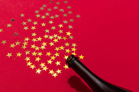 Champagne bottle with golden stars confetti isolated over red background. Happy New Yearの写真素材