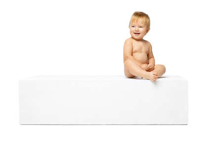 Portrait of little cute toddler boy, baby in diaper sitting isolated over white studio background. Side viewの写真素材