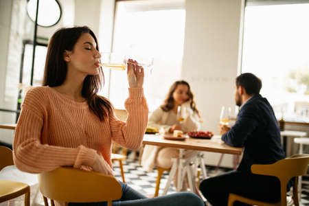 Cropped portrait of beautiful woman drinking white wine, having event celebration with wriends at cafe on warm sunny dayの写真素材
