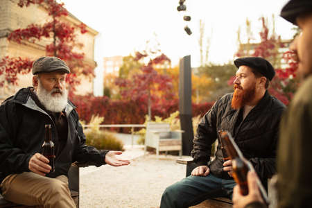 Group of male friends spending time together outdoors on warm autumn day. Drinking lager beer
