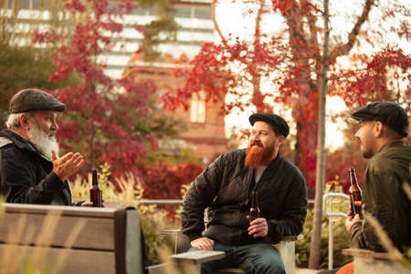 Group of male friends spending time together outdoors on warm autumn day. Drinking lager beer