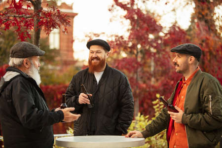 Group of male friends spending time together outdoors on warm autumn day. Drinking lager beer