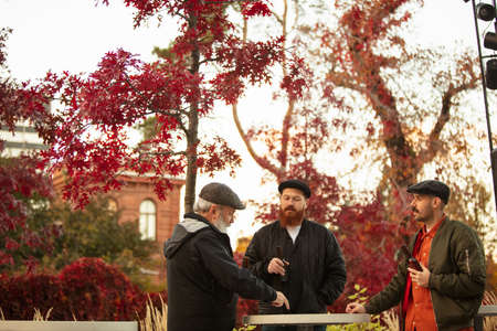 Group of male friends spending time together outdoors on warm autumn day. Drinking beerの写真素材