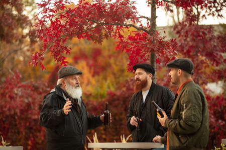 Group of male friends spending time together outdoors on warm autumn day. Drinking beer
