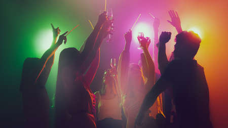 Group of young, active people at the night club, party dancing in neon lights