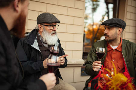 Group of men, friends having a meeting at cafe on warm autumn day. Drinking red wine, clinking glassesの写真素材