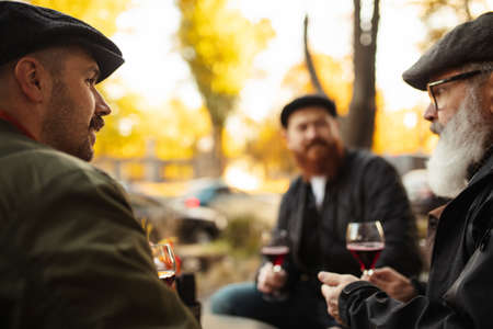 Group of men, friends having a meeting at cafe on warm autumn day. Drinking red wine, clinking glassesの写真素材