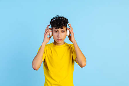 Cropped portrait of young boy in yellow T-shirt wearing headphones isolated over blue backgroundの写真素材