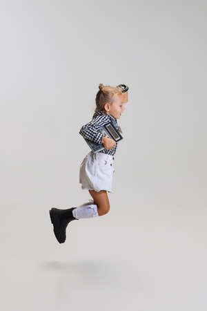 Full-length side view portrait of little cute girl, child in skirt and checkered shirt jumping...