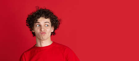 Cropped portrait of young man in casual cloth making faces isolated over red background. Flyerの写真素材